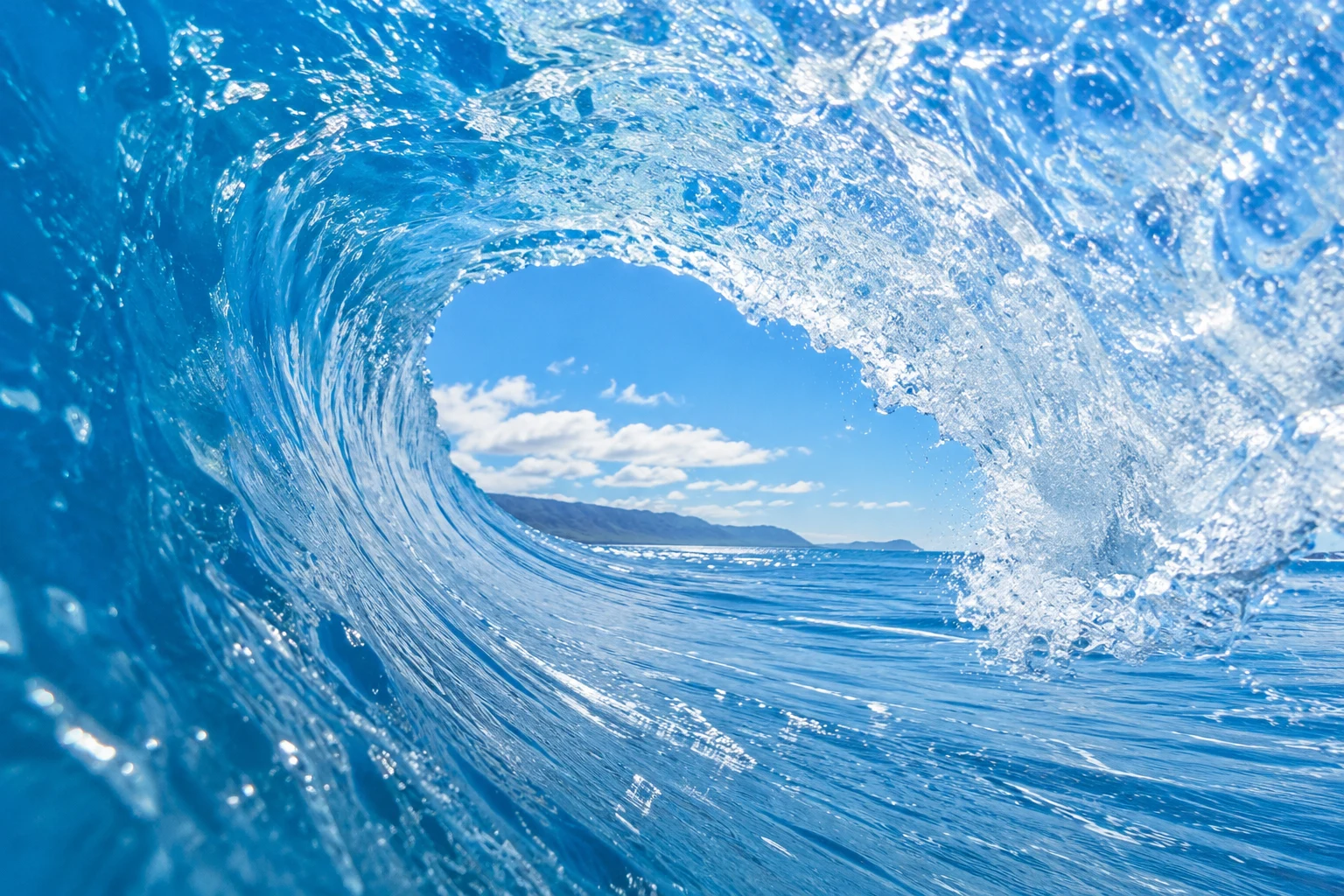 Looking from inside a sunlit blue wave as it curls into an ocean barrel